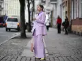 Elegancka kobieta w garniturze w kolorze liliowym, z transparentną torbą, idzie ulicą.