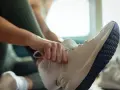 Dłoń zawiązuje sznurówki w białych butach sportowych. Może to być znak, że zaraz zacznie się trening, ale czy te za duże buty nie sprawią problemu?