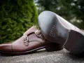 Eleganckie brązowe buty z podwójnymi klamrami, wykonane z wysokiej jakości kruponu. Widoczna podeszwa z logo marki.