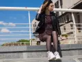 Dziewczyna w eleganckiej sukience i sportowych butach siedzi na deskorolce na schodach.