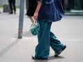 Kobieta w szerokich spodniach w kolorze petrol i dżinsowej bluzce z tie-dye, niosąca turkusową torebkę.