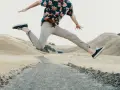 Mężczyzna w kwiecistej koszuli i beżowych chinosach skacze na ścieżce. Idealne buty do chinosów to czarne trampki.