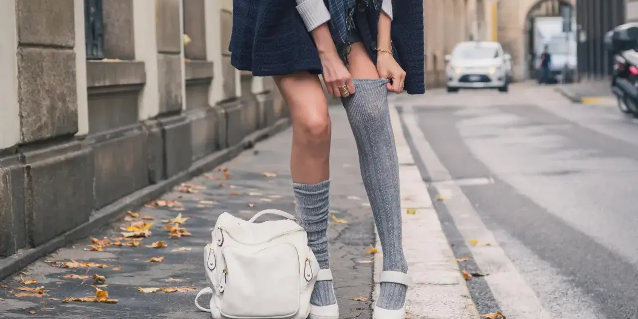 Stylizacja z długimi skarpetkami damskimi. Szare, prążkowane skarpetki do połowy uda, biały plecak i mokasyny.