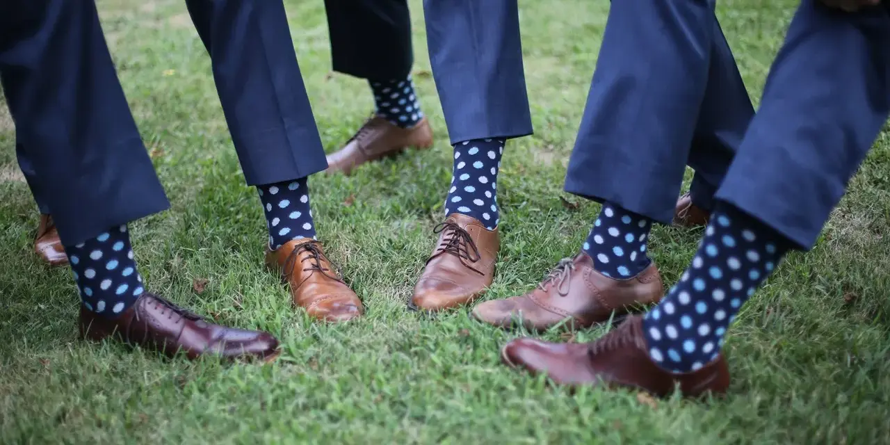 Elegancki granatowy garnitur i brązowe buty, a do tego zabawne skarpetki w kropki. Idealny zestaw na letnie wesele.