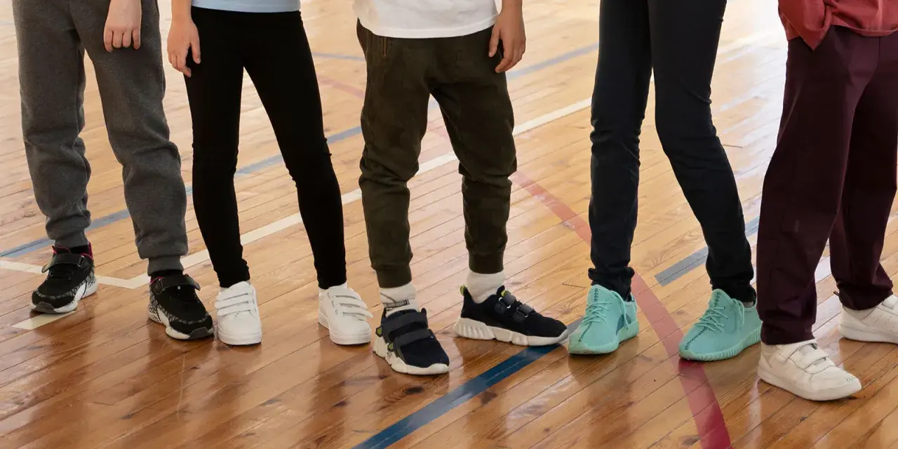 Dzieci na sali gimnastycznej, zastanawiające się, jakie buty na WF do szkoły wybrać. Różne modele sportowego obuwia na drewnianej podłodze.