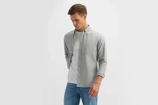 Modny mężczyzna w szarej koszuli i jeansach, prezentujący swobodny, ale stylowy wygląd.
