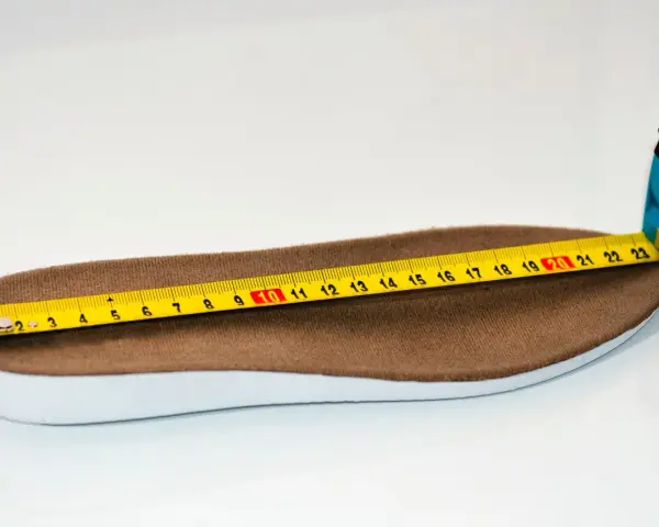 Miarka krawiecka mierzy brązową wkładkę. Długość wkładki wynosi około 23 cm, co odpowiada rozmiarowi 38.