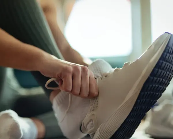 Dłoń zawiązuje sznurówki w białych butach sportowych. Może to być znak, że zaraz zacznie się trening, ale czy te za duże buty nie sprawią problemu?