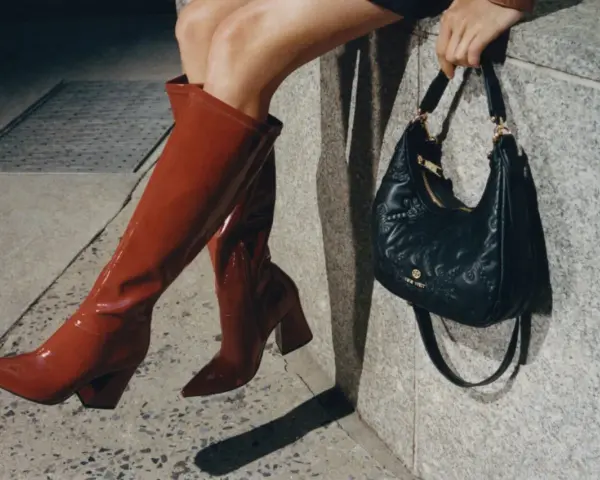 Kobieta w czerwonych kozakach i pikowanej torebce z logo Nine West. Nine West to znana marka obuwia i akcesoriów.