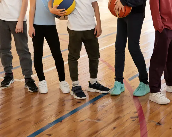 Dzieci na sali gimnastycznej, zastanawiające się, jakie buty na WF do szkoły wybrać. Różne modele sportowego obuwia na drewnianej podłodze.