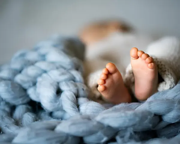 Malutkie stópki dziecka, rozmiar 74 sugeruje wiek około 6-9 miesięcy. Otulone w miękkie kocyki.