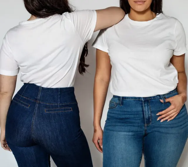 Dwie kobiety w białych T-shirtach i jeansach. Jedna stoi tyłem, druga przodem, opierając rękę na ramieniu koleżanki. Ich sylwetka v podkreślona przez dopasowane spodnie.