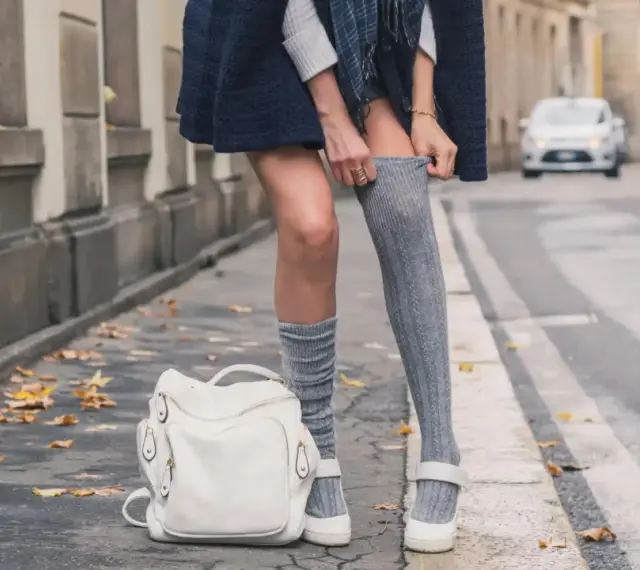 Stylizacja z długimi skarpetkami damskimi. Szare, prążkowane skarpetki do połowy uda, biały plecak i mokasyny.