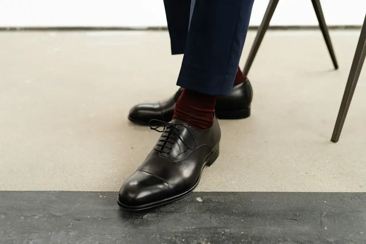 Eleganckie, czarne oksfordy i bordowe skarpety – idealne buty do czarnego garnituru na specjalne okazje.
