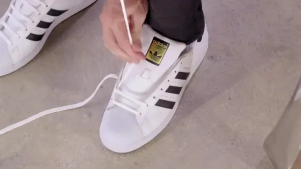 Pokazuję, jak wiązać sznurówki w adidasach Superstar. Białe sznurówki przeplatane przez czarne paski.