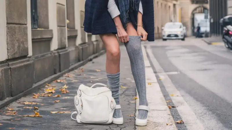 Stylizacja z długimi skarpetkami damskimi. Szare, prążkowane skarpetki do połowy uda, biały plecak i mokasyny.